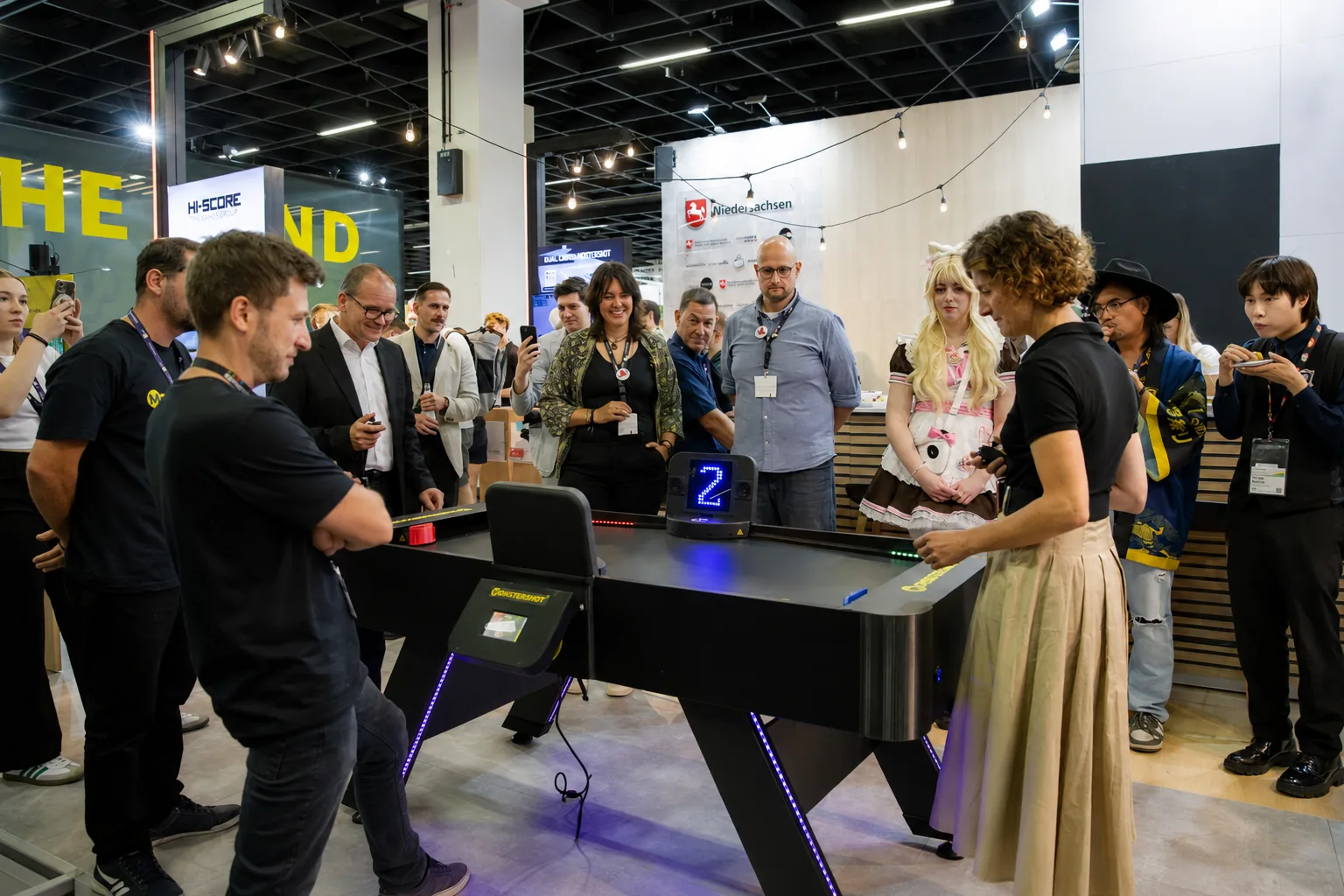 Monstershot®-Spieltisch auf der Gamescom, zwei Spieler am Tisch, Besucher schauen zu und filmen