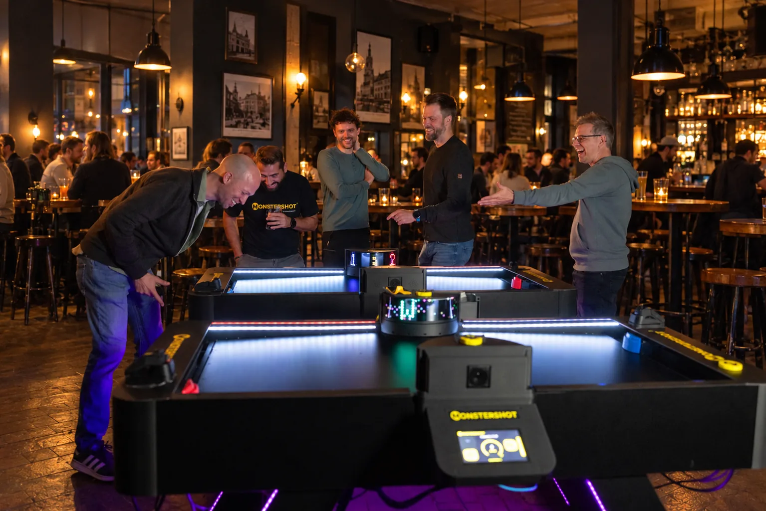 Gruppe spielt und jubelt abends an zwei Monstershot®-Spieltischen in einer Bar