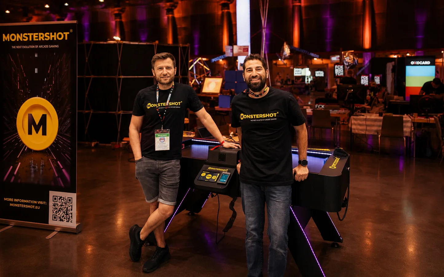 Die Monstershot®-Gründer Maan und Alexander an ihrem Messestand mit Spieltisch und Roll-up-Banner