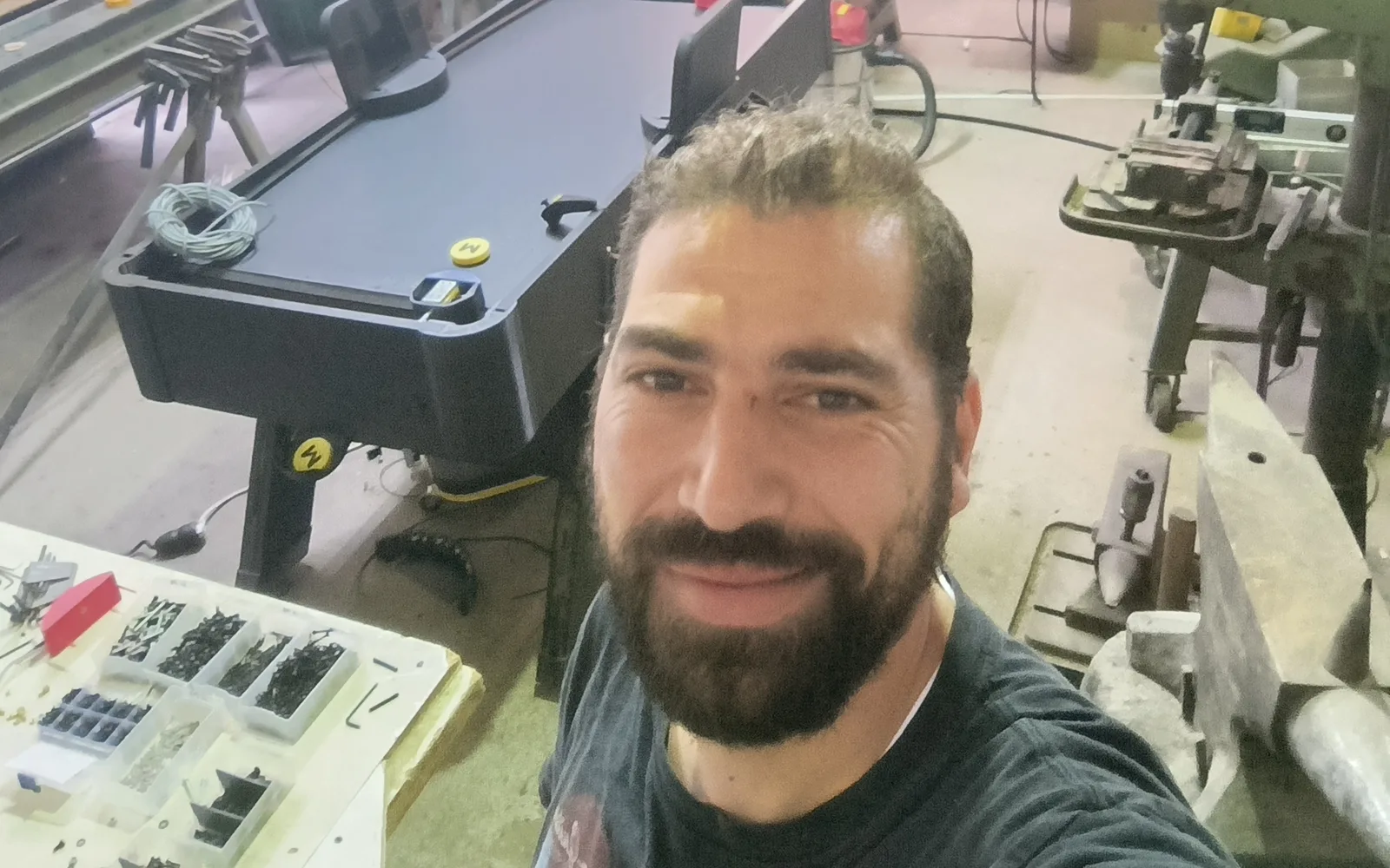 Selfie von Mitgründer Maan in der Werkstatt, dahinter ein Monstershot®-Tisch im Aufbau